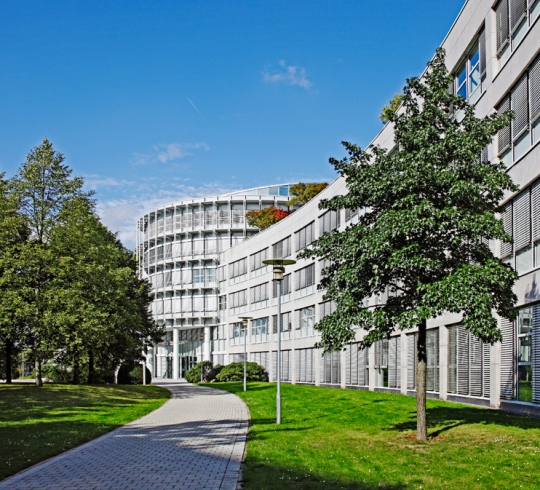 Moderne Bürogebäude von Heise RegioConcept mit geschwungenen Fassaden und Bäumen im Vordergrund an einem sonnigen Tag.